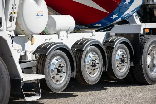 Close-up of reconfigured auxiliary axles with black fenders on an Oshkosh S-Series front discharge mixer truck.