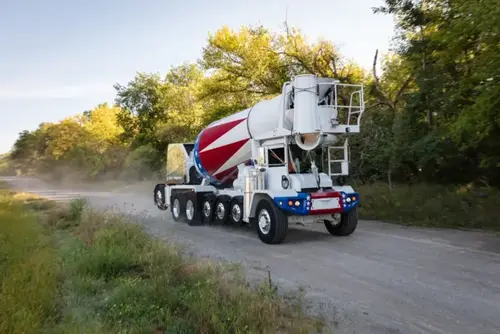 An Oshkosh S-Series front discharge mixer truck with a patriotic drum drives along a gravel road.