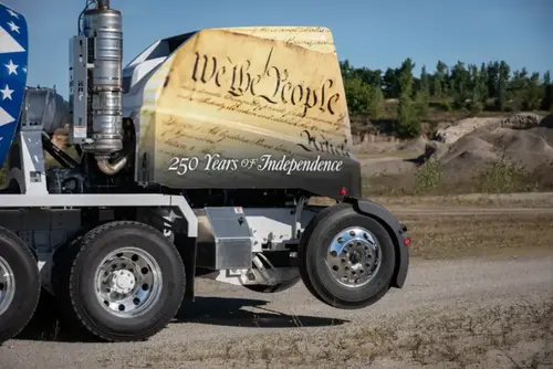 Oshkosh S-Series concrete mixer truck with a high-lift tag axle and patriotic We the People graphic wrap.